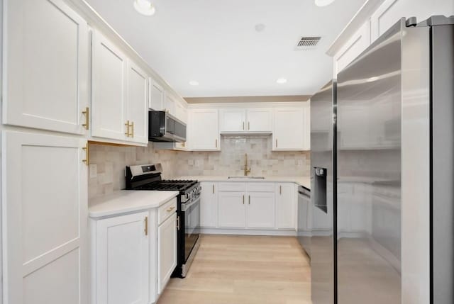 kitchen with tasteful backsplash, stainless steel appliances, sink, light hardwood / wood-style floors, and white cabinetry