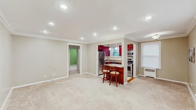 interior space with a breakfast bar, radiator heating unit, ornamental molding, and appliances with stainless steel finishes