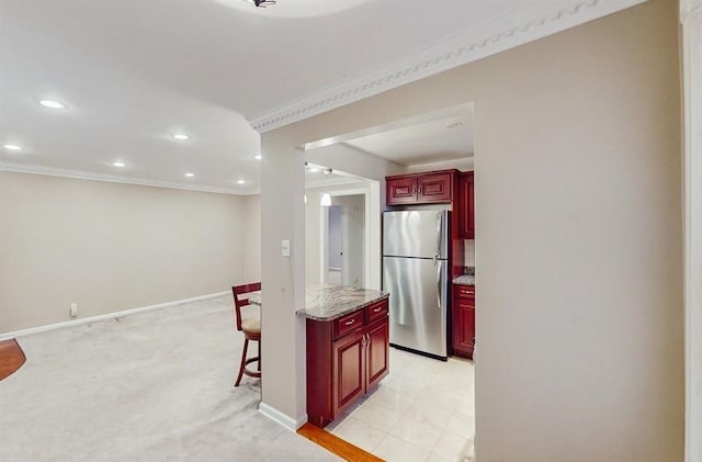 kitchen featuring a breakfast bar, light stone countertops, ornamental molding, light colored carpet, and stainless steel refrigerator