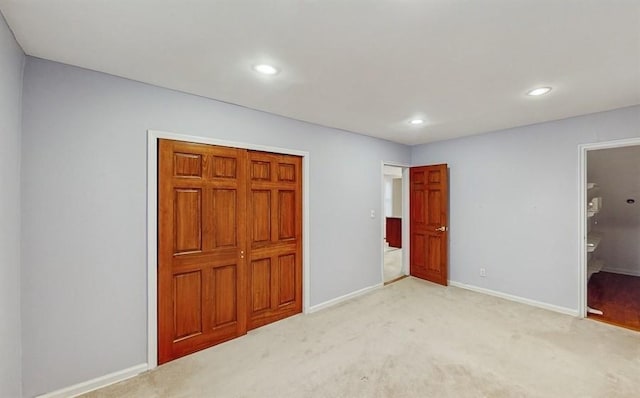 unfurnished bedroom with ensuite bathroom, light carpet, and a closet