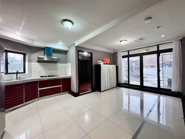 kitchen with tasteful backsplash, wall chimney range hood, light tile patterned floors, and gas cooktop