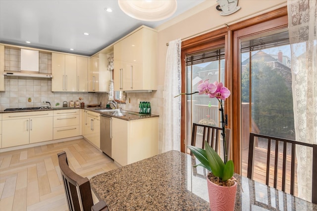 kitchen featuring cream cabinetry, decorative backsplash, stainless steel appliances, and wall chimney exhaust hood