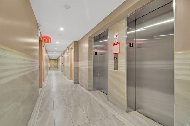 corridor with elevator, light tile patterned floors, and tile walls