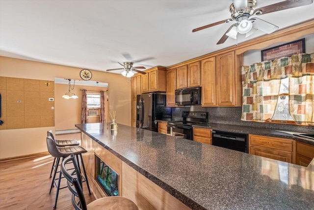 kitchen with tasteful backsplash, black appliances, pendant lighting, light hardwood / wood-style floors, and a breakfast bar area