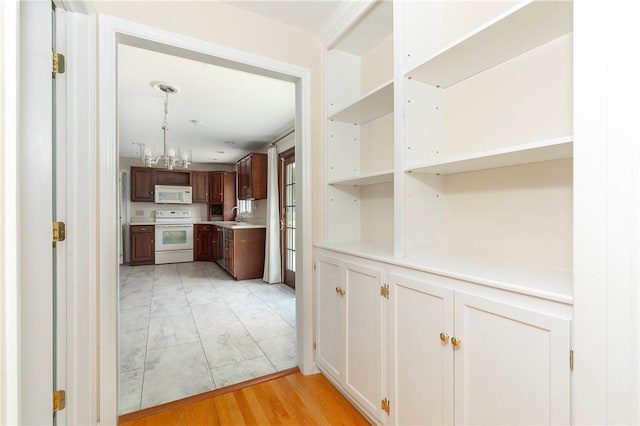 kitchen with white appliances, light hardwood / wood-style floors, a notable chandelier, and sink