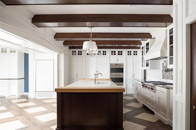 kitchen featuring custom exhaust hood, a center island with sink, sink, appliances with stainless steel finishes, and decorative light fixtures