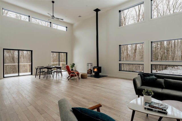 living room with a wood stove, ceiling fan, light hardwood / wood-style flooring, and a high ceiling