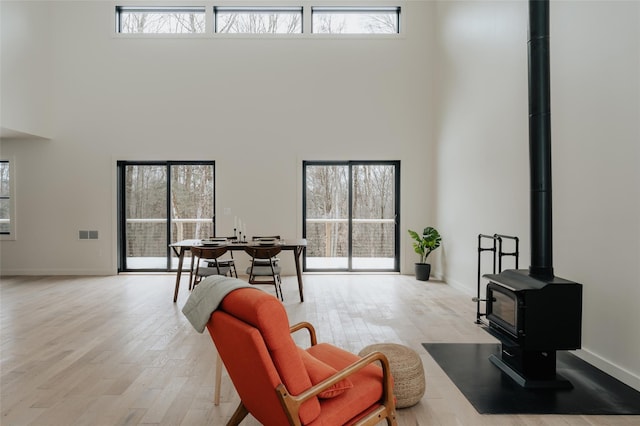 living room featuring a high ceiling, light hardwood / wood-style floors, a wood stove, and a healthy amount of sunlight