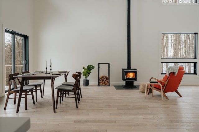 dining area with a wood stove, light hardwood / wood-style floors, and a high ceiling