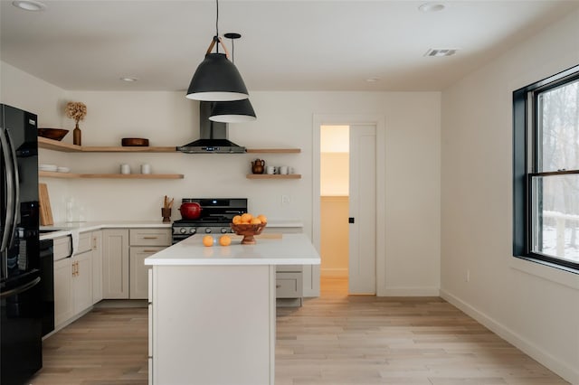 kitchen featuring wall chimney exhaust hood, black appliances, light hardwood / wood-style flooring, white cabinetry, and hanging light fixtures