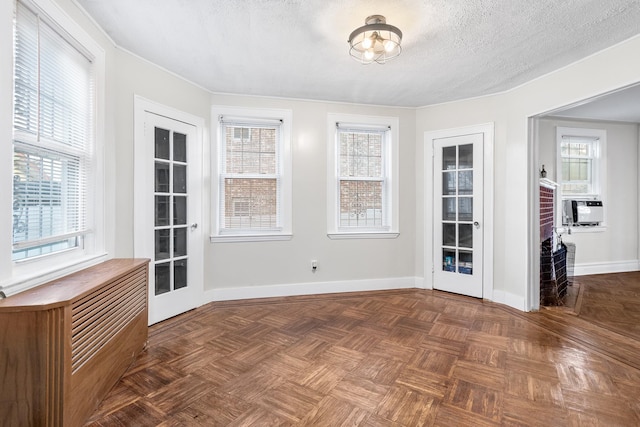 empty room with french doors, plenty of natural light, dark parquet floors, and a textured ceiling