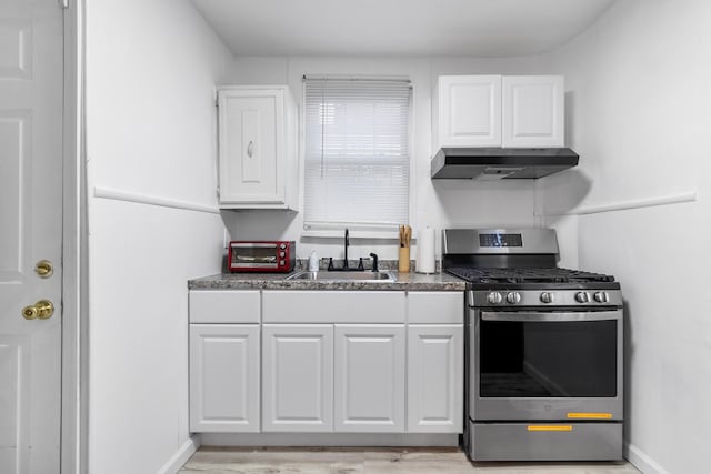 kitchen with stainless steel gas stove, white cabinetry, and sink