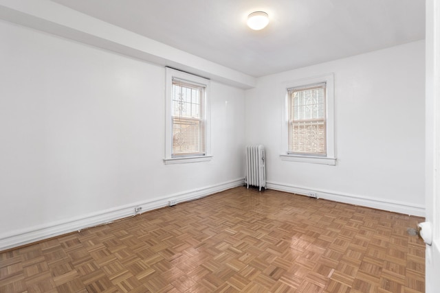 unfurnished room with radiator heating unit, light parquet flooring, and plenty of natural light