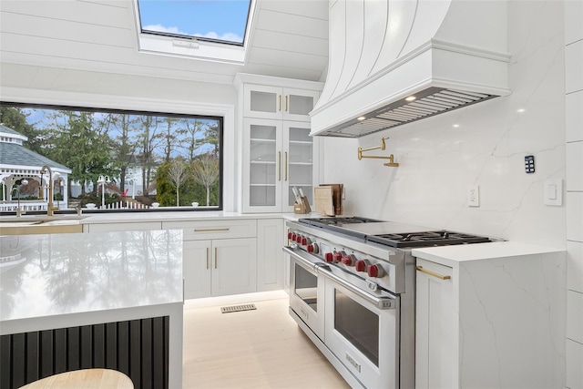 kitchen featuring luxury stove, white cabinetry, custom exhaust hood, light stone countertops, and sink