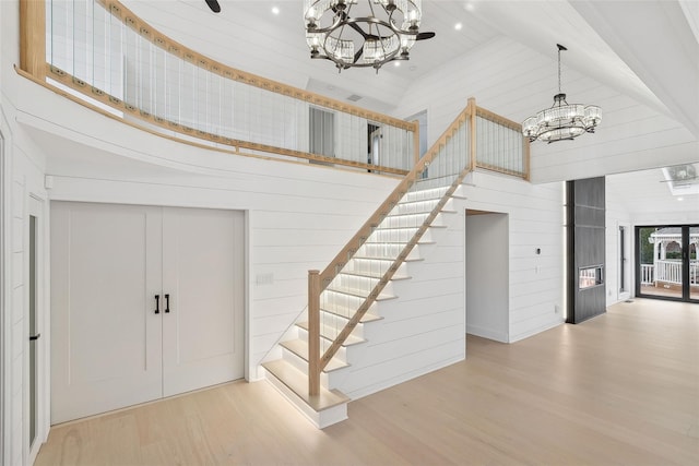 staircase featuring wood-type flooring, a notable chandelier, wood walls, and a towering ceiling