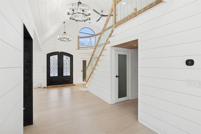 foyer entrance featuring an inviting chandelier, wooden walls, french doors, high vaulted ceiling, and light hardwood / wood-style flooring