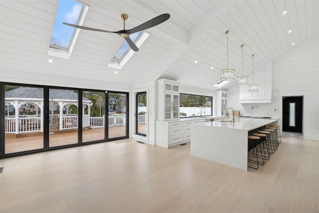 kitchen featuring a skylight, white cabinetry, ceiling fan, a kitchen island with sink, and high vaulted ceiling