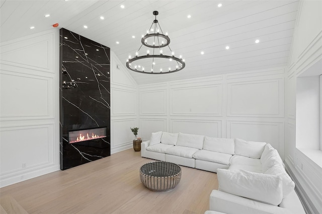 living room featuring vaulted ceiling, a high end fireplace, an inviting chandelier, and light hardwood / wood-style floors