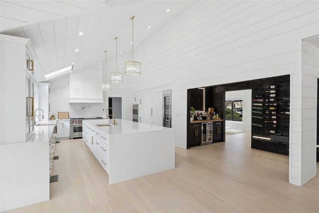 kitchen with wine cooler, pendant lighting, white cabinetry, a kitchen island with sink, and high vaulted ceiling