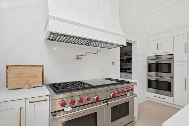 kitchen with white cabinets, appliances with stainless steel finishes, light hardwood / wood-style flooring, and custom range hood