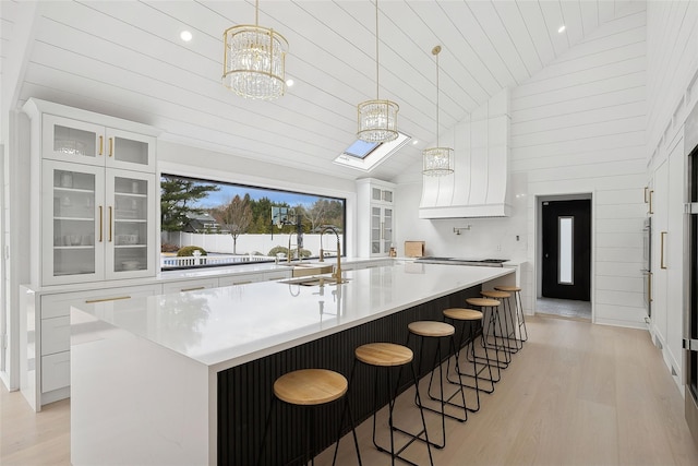 kitchen with an inviting chandelier, white cabinetry, a skylight, pendant lighting, and a large island with sink