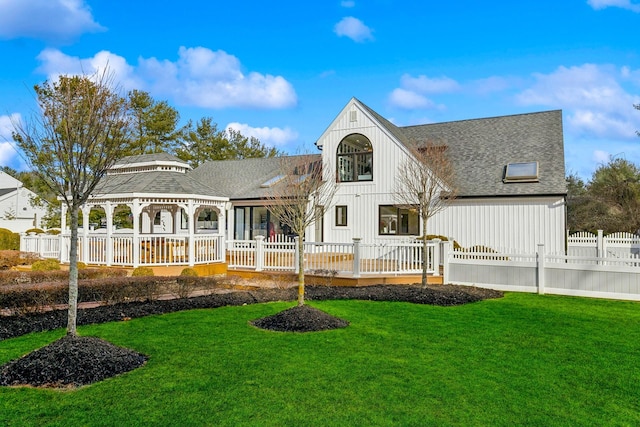 rear view of house featuring a yard, a fenced front yard, a shingled roof, and a gazebo