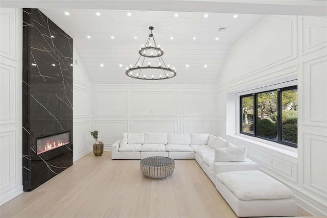 living room with lofted ceiling, light wood-style flooring, a decorative wall, a high end fireplace, and an inviting chandelier