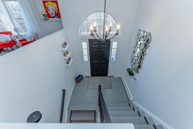 entryway with a chandelier, a towering ceiling, baseboard heating, and a healthy amount of sunlight