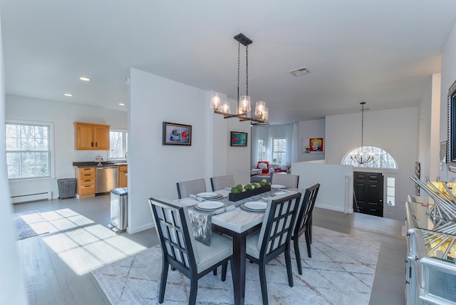 dining room with plenty of natural light, light hardwood / wood-style flooring, a baseboard heating unit, and an inviting chandelier