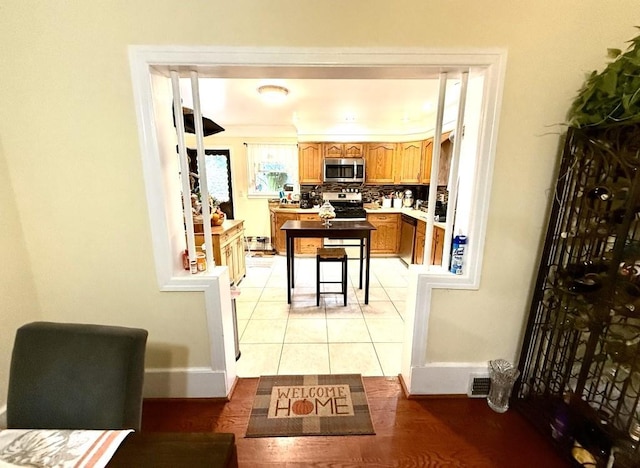 kitchen with appliances with stainless steel finishes, light countertops, brown cabinetry, light tile patterned floors, and backsplash