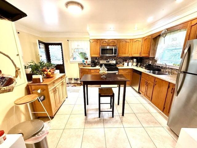 kitchen with a healthy amount of sunlight, appliances with stainless steel finishes, brown cabinets, a sink, and ornamental molding