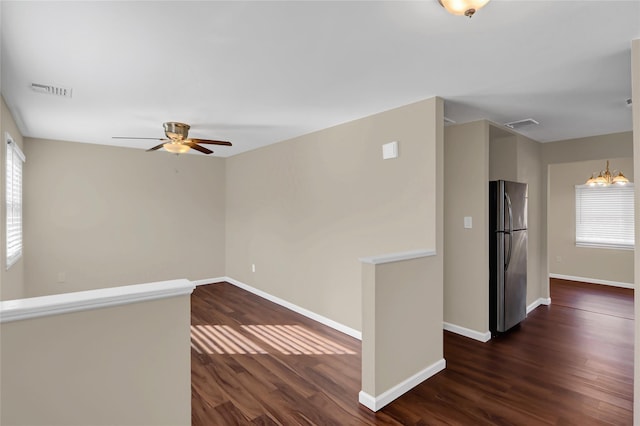 empty room featuring a wealth of natural light, dark wood-type flooring, and ceiling fan with notable chandelier