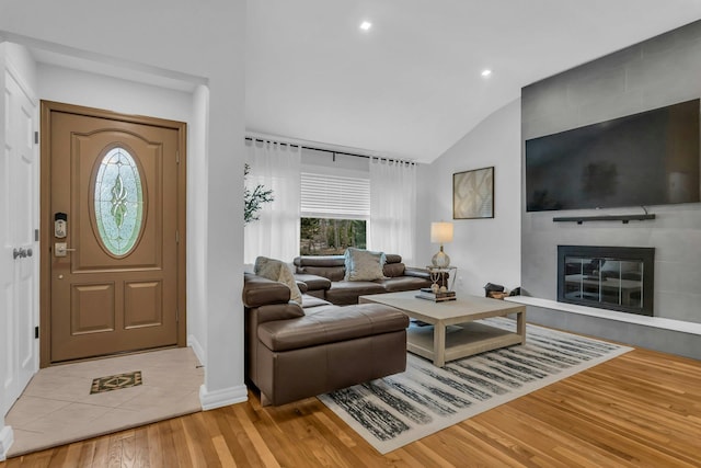 living room featuring light hardwood / wood-style floors, vaulted ceiling, and a tiled fireplace