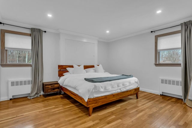 bedroom with radiator heating unit, light hardwood / wood-style floors, and multiple windows