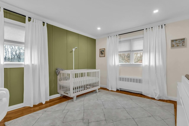 unfurnished bedroom featuring light hardwood / wood-style floors, a crib, radiator heating unit, and crown molding