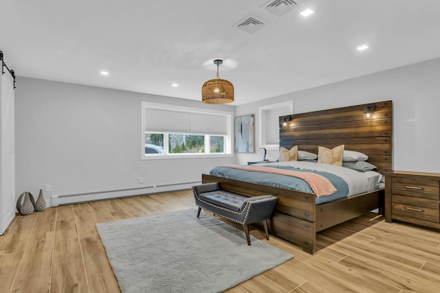 bedroom featuring a barn door, baseboard heating, and light hardwood / wood-style flooring