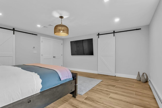 bedroom featuring a barn door, light hardwood / wood-style flooring, and baseboard heating