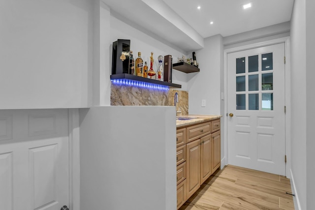 bar featuring light brown cabinets, light hardwood / wood-style floors, and sink