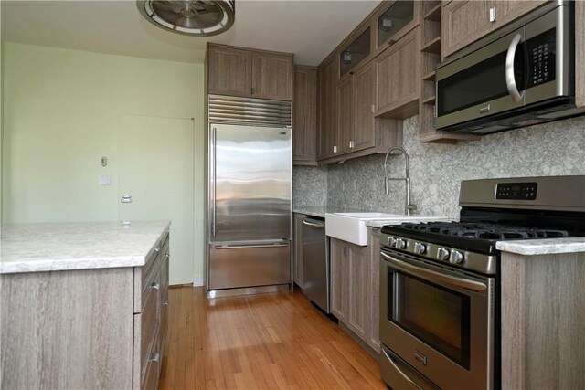 kitchen with tasteful backsplash, sink, stainless steel appliances, and light hardwood / wood-style floors