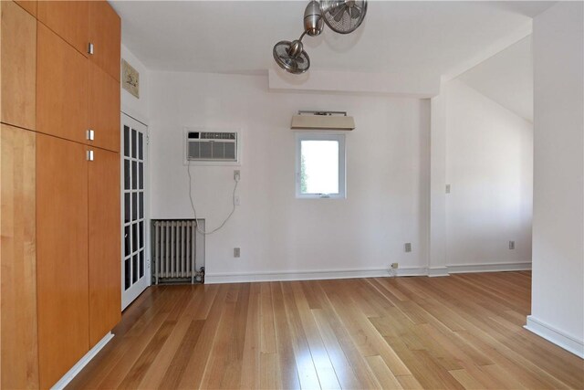 unfurnished room with light hardwood / wood-style flooring, a wall mounted air conditioner, and radiator heating unit