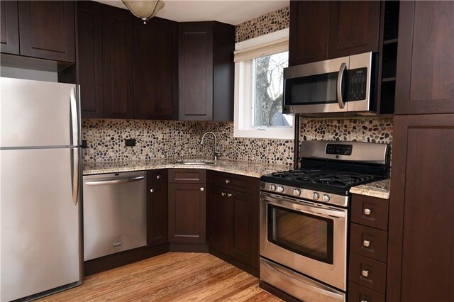 kitchen featuring appliances with stainless steel finishes, light wood-type flooring, tasteful backsplash, light stone counters, and sink