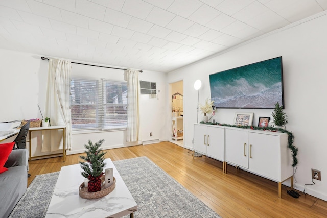 living room with baseboards, a wall mounted air conditioner, and light wood finished floors