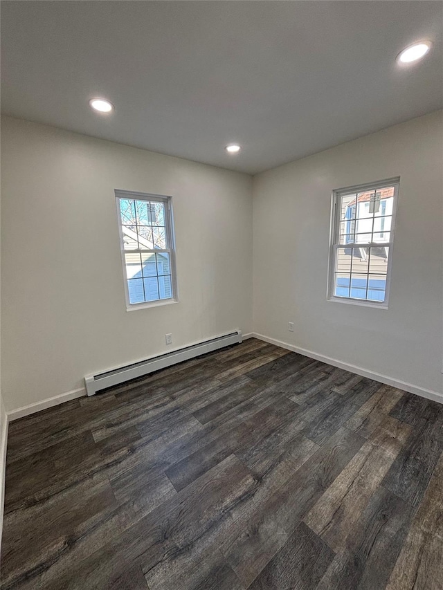 empty room featuring a baseboard heating unit, plenty of natural light, and dark wood-style floors