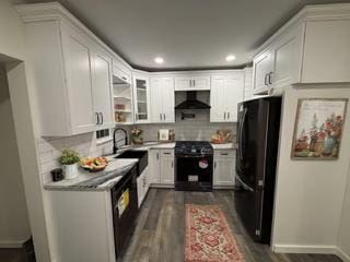 kitchen with dark wood-style flooring, decorative backsplash, white cabinetry, black appliances, and extractor fan