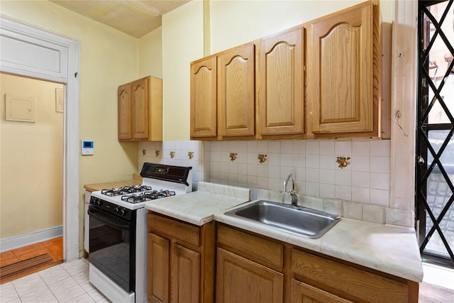 kitchen featuring tasteful backsplash, white range with gas cooktop, sink, and light tile patterned floors