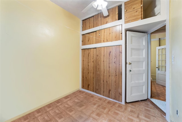 spare room featuring light parquet floors, ceiling fan, and wooden walls