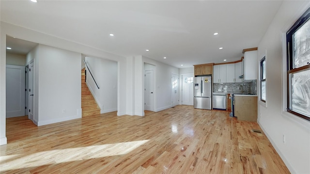 kitchen featuring sink, appliances with stainless steel finishes, decorative backsplash, white cabinets, and light wood-type flooring