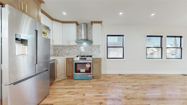 kitchen with white cabinetry, wall chimney range hood, tasteful backsplash, appliances with stainless steel finishes, and light wood-type flooring