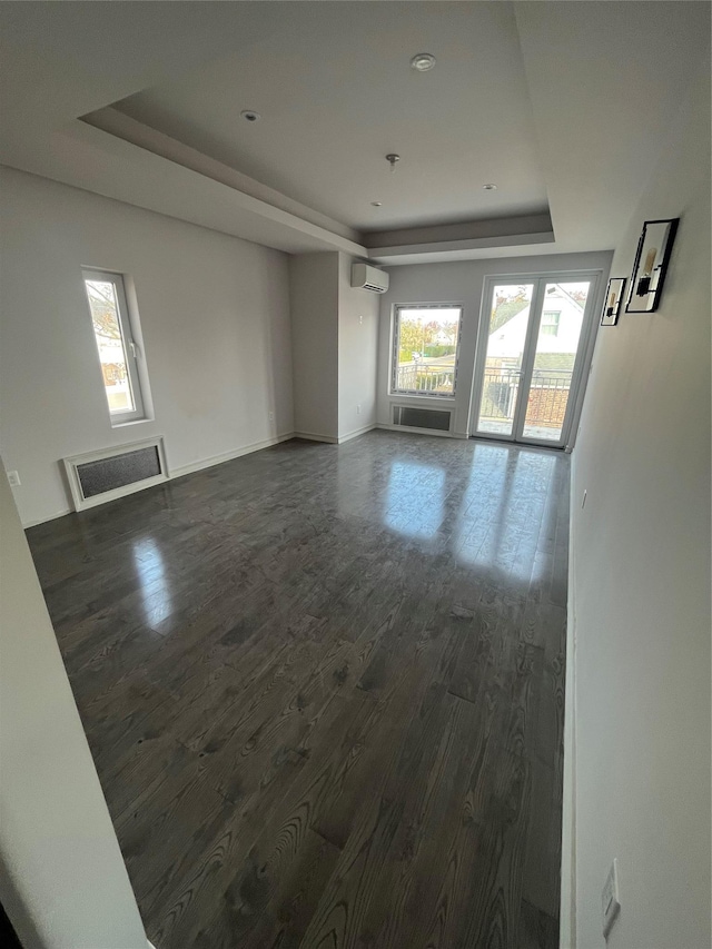 unfurnished room with a tray ceiling, a wealth of natural light, dark hardwood / wood-style flooring, and a wall mounted air conditioner