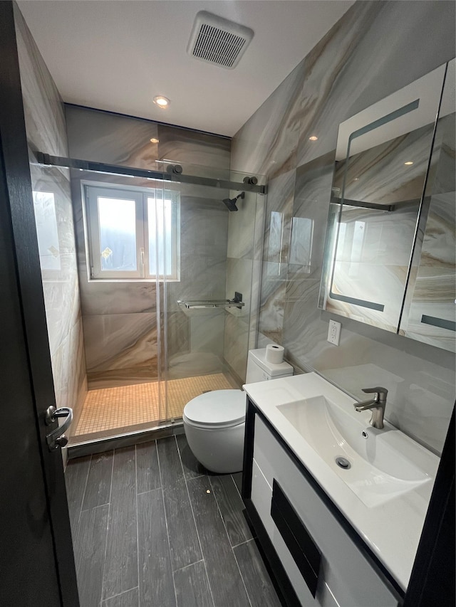 bathroom featuring a shower with door, vanity, tile walls, and toilet